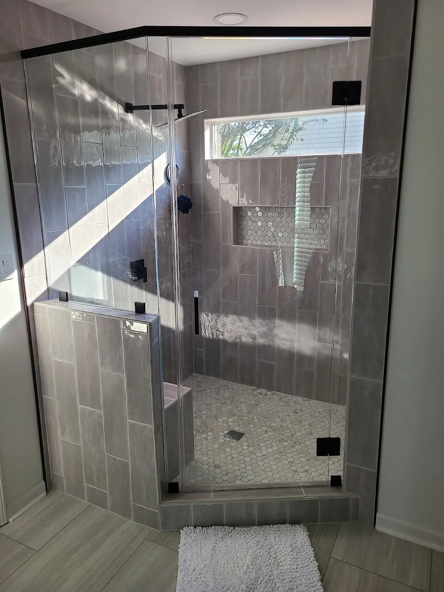 Frameless glass walk-in shower with large-format gray tile and a corner bench