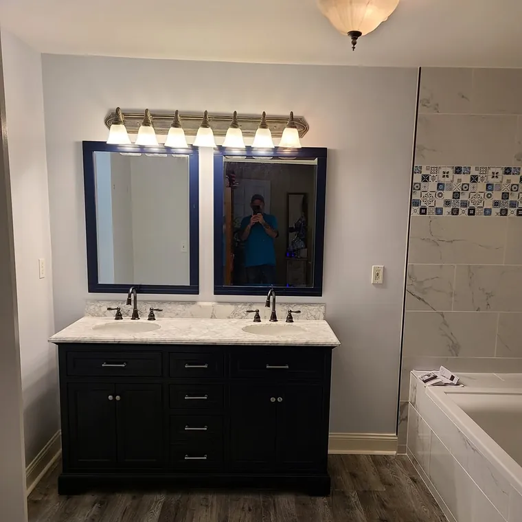 Bathroom remodel with a black double vanity, framed mirrors and a tiled tub surround