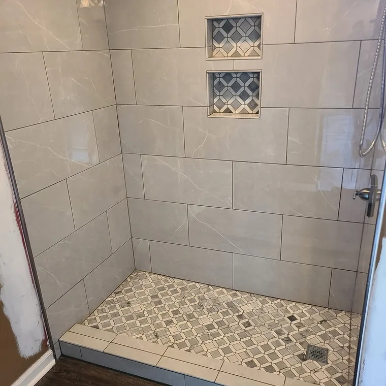 Walk-in tile shower with a mosaic pebble floor and built-in shampoo niche