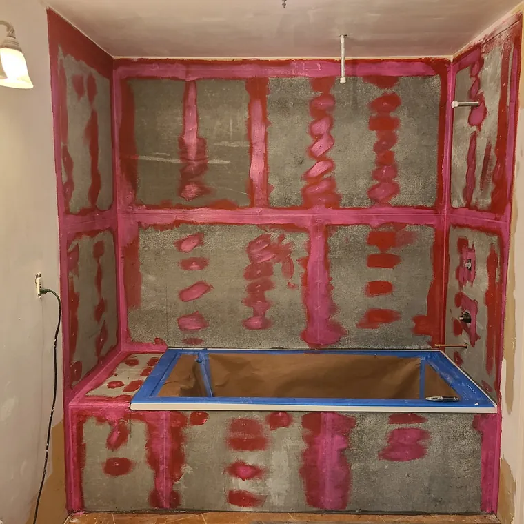 Red waterproofing membrane applied over a shower pan and walls before tile